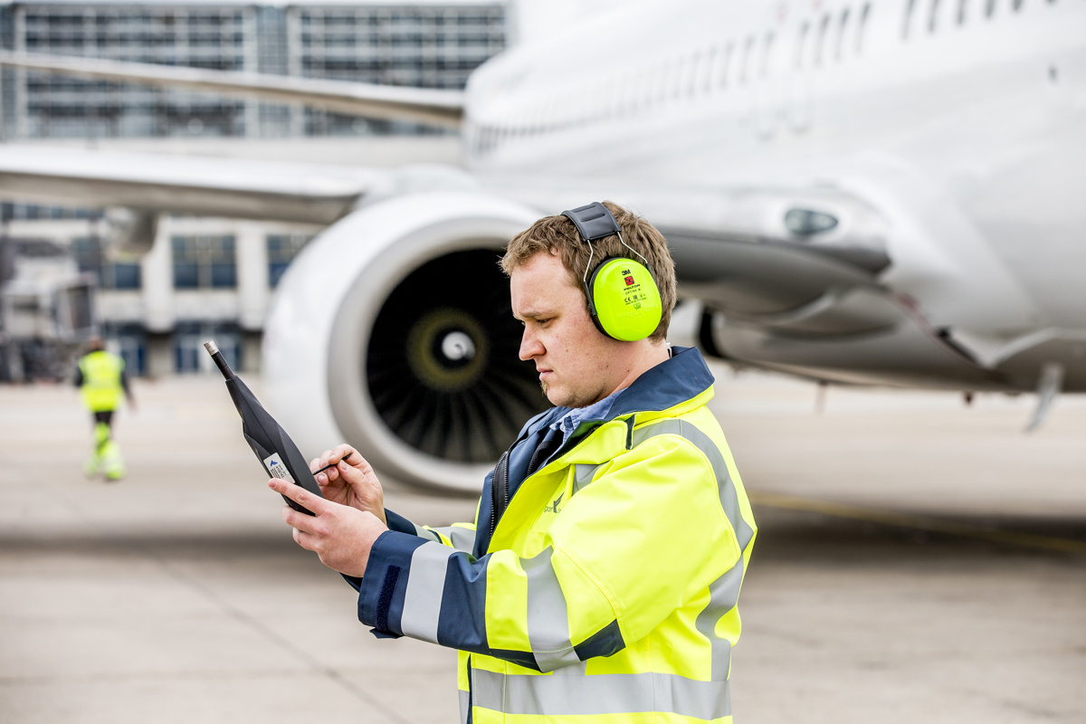 Mitarbeiter misst den Schall auf dem Vorfeld neben einem Flugzeug